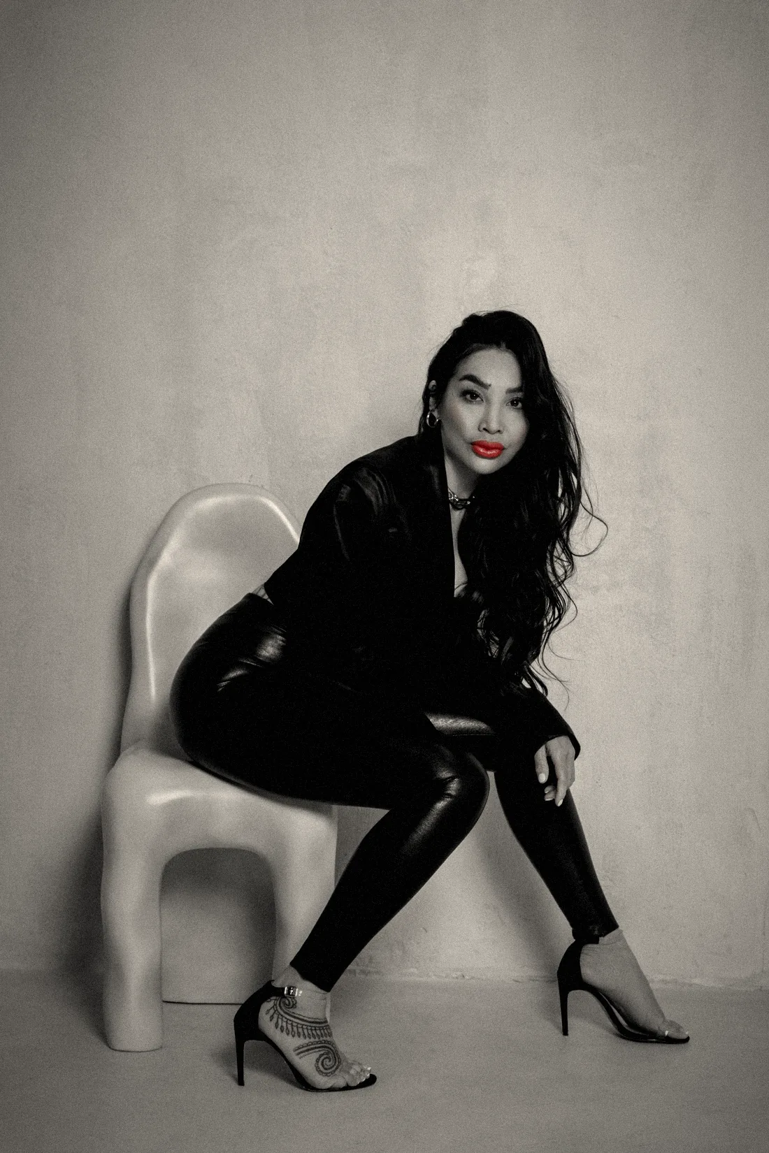 Chayenne Mallari leaning forward on a sculptural white chair, black leather and red lips