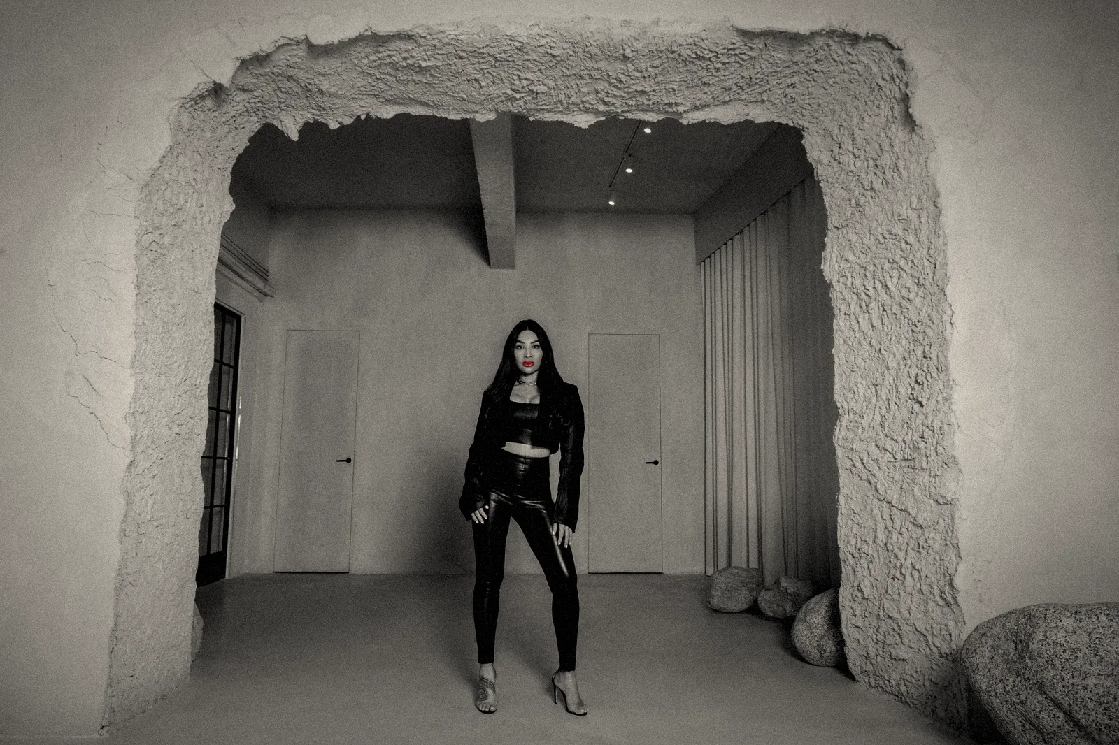 Chayenne Mallari standing in a raw plaster archway in black leather